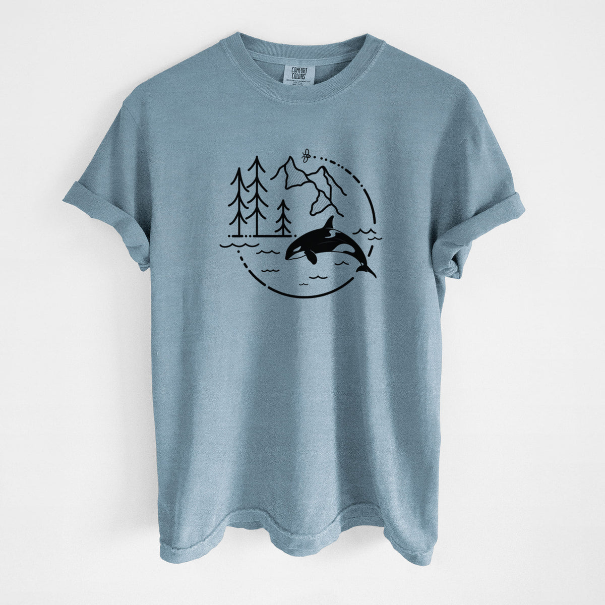 Steel blue Comfort Colors t-shirt laid flat, printed with a black line art circle connecting pine trees, mountains, a bee and an orca leaping from ocean waves.