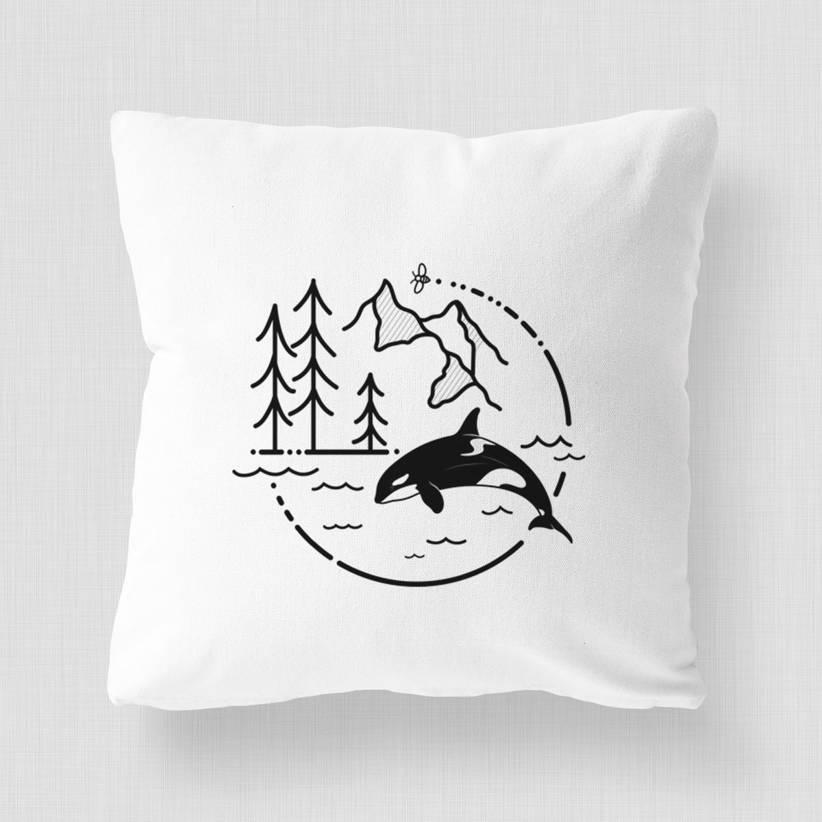 White pillow cover printed with a black line art circle connecting pine trees, mountains, a bee and an orca leaping from ocean waves.
