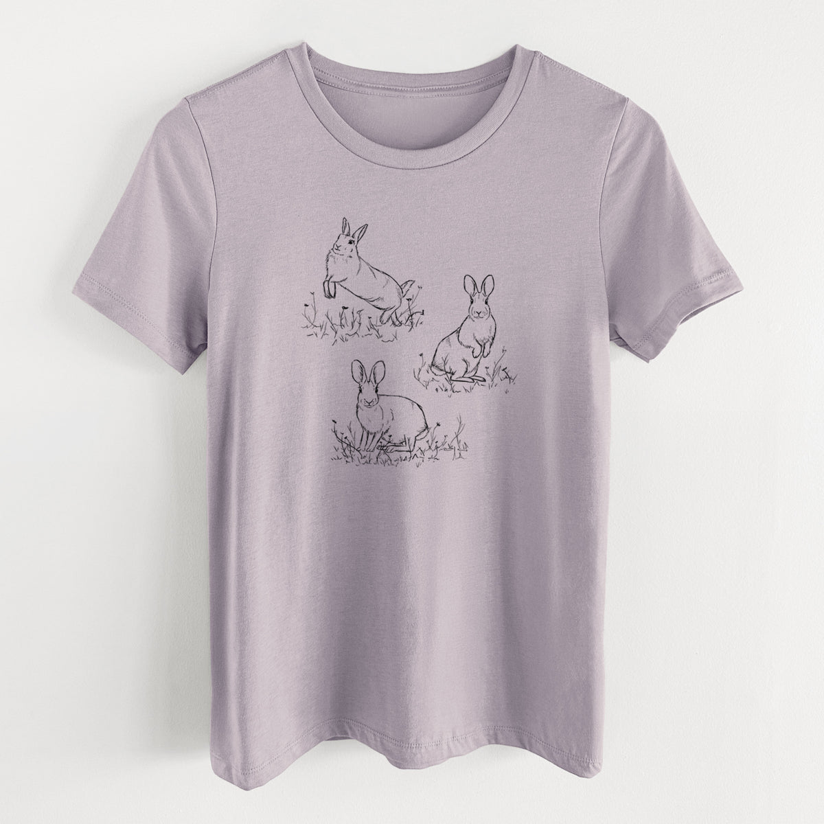Light violet women's relaxed fit cotton t-shirt laid flat, printed with a black ink illustration of three cottontail rabbits among grass and flowers.