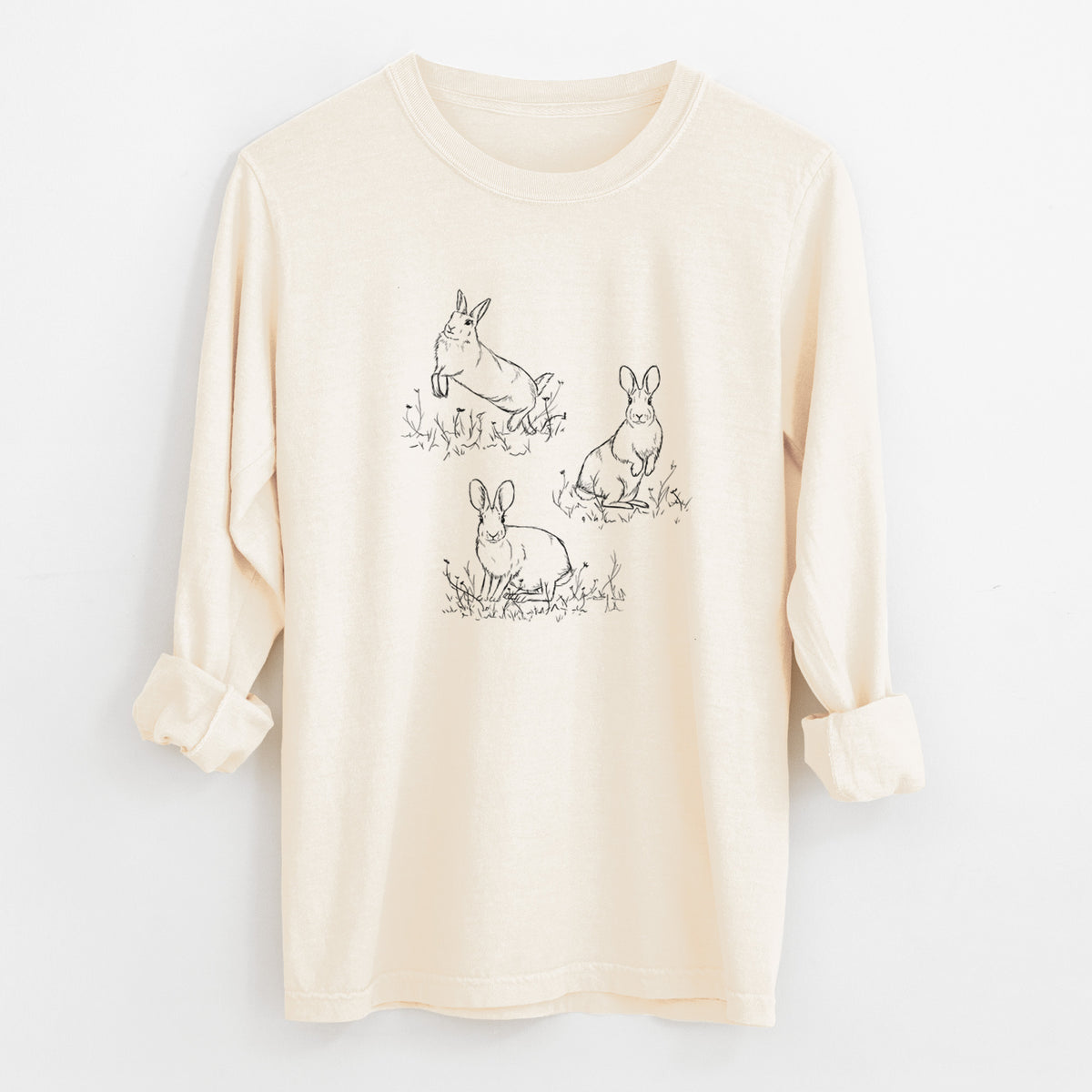 Ivory Comfort Colors long sleeve shirt laid flat with the cuffs rolled, printed with a black ink illustration of three cottontail rabbits among grass and flowers.