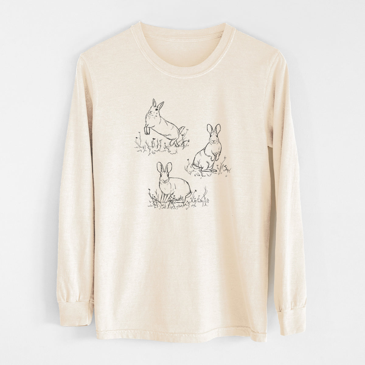 Ivory Comfort Colors long sleeve shirt laid flat, printed with a black ink illustration of three cottontail rabbits among grass and flowers.