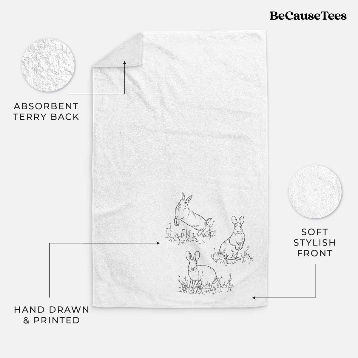 White hand towel printed with a black ink illustration of three cottontail rabbits among grass and flowers.