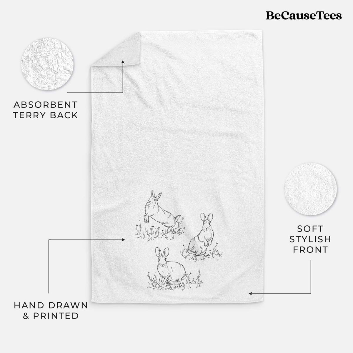 White hand towel printed with a black ink illustration of three cottontail rabbits among grass and flowers.
