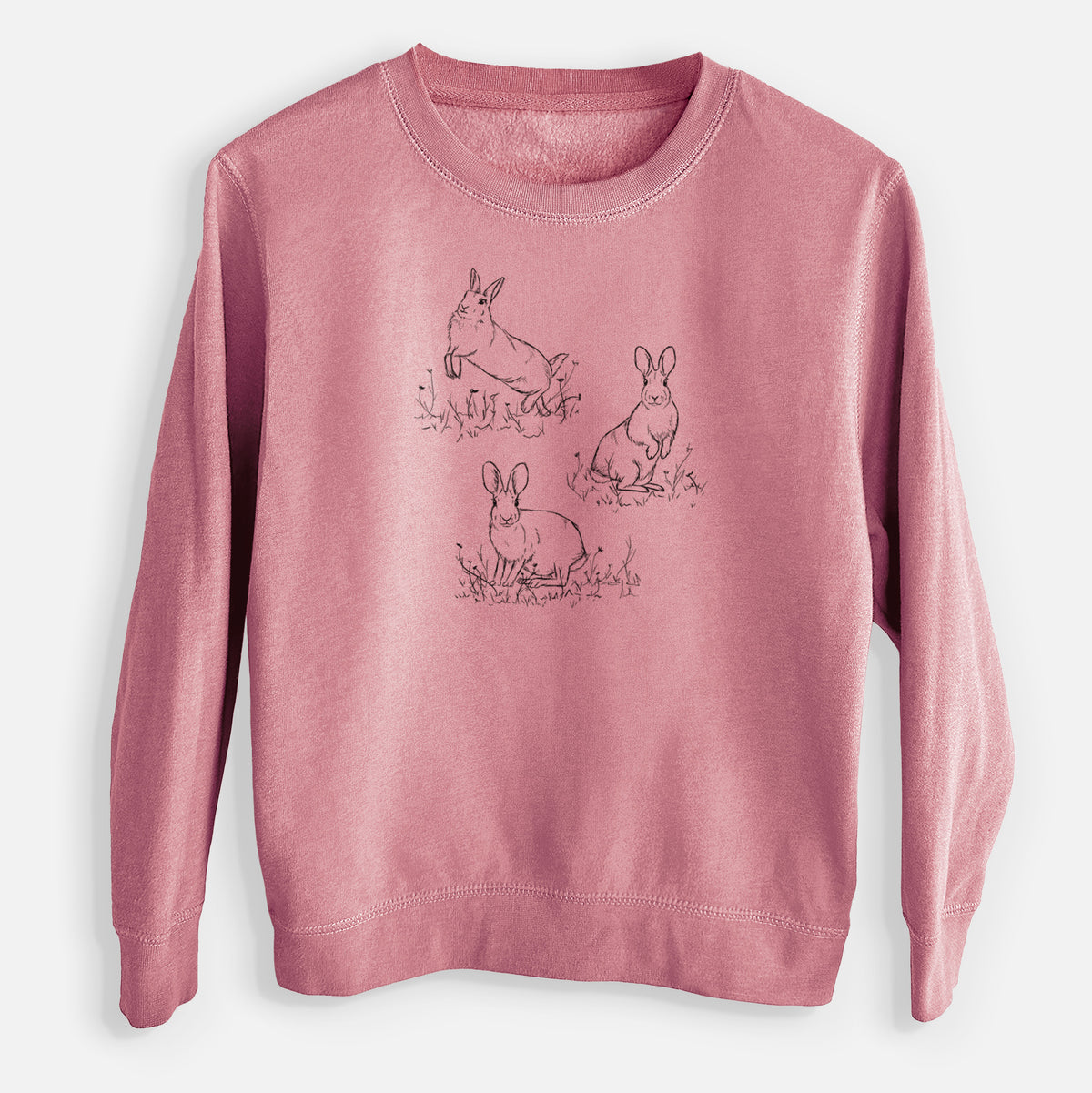 Mauve pink youth crewneck sweatshirt laid flat, printed with a black ink illustration of three cottontail rabbits among grass and flowers.