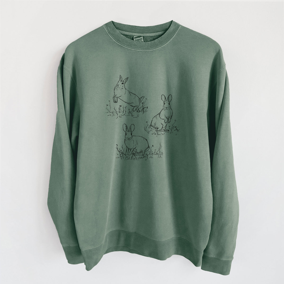 Alpine green pigment dyed crewneck sweatshirt laid flat, printed with a black ink illustration of three cottontail rabbits among grass and flowers.