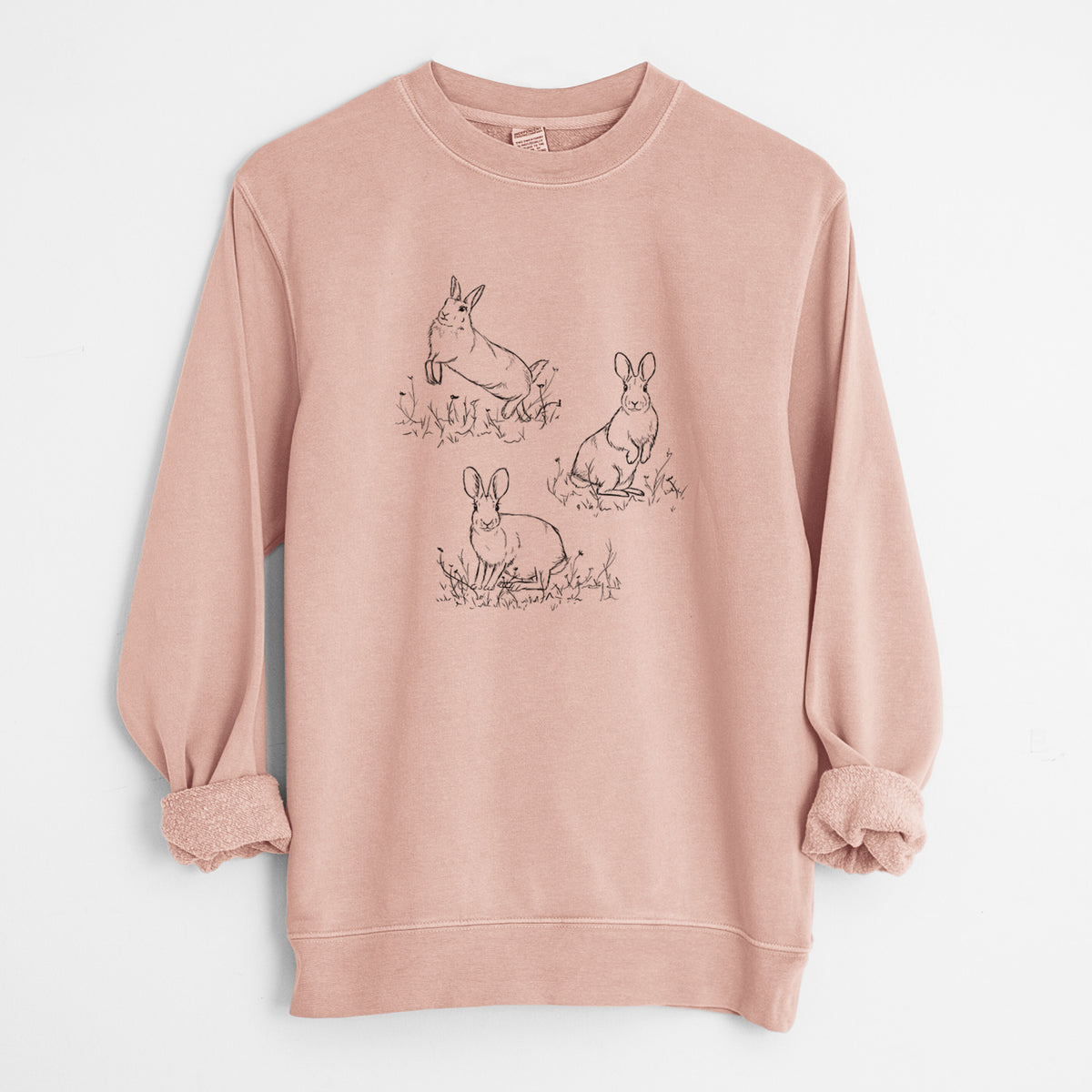Dusty pink pigment dyed crewneck sweatshirt laid flat with the sleeves rolled, printed with a black ink illustration of three cottontail rabbits among grass and flowers.