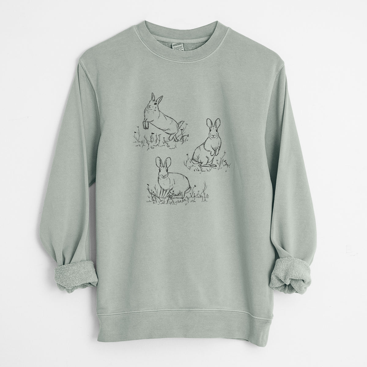Sage green pigment dyed crewneck sweatshirt laid flat with the sleeves rolled, printed with a black ink illustration of three cottontail rabbits among grass and flowers.
