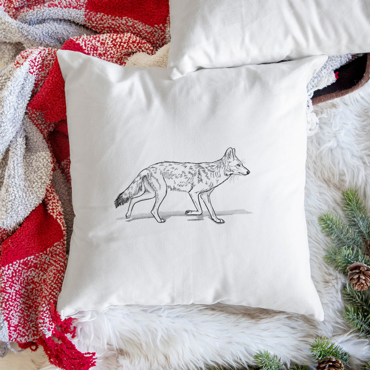 White pillow cover printed with a black ink illustration of a coyote trotting, on a woven chair.