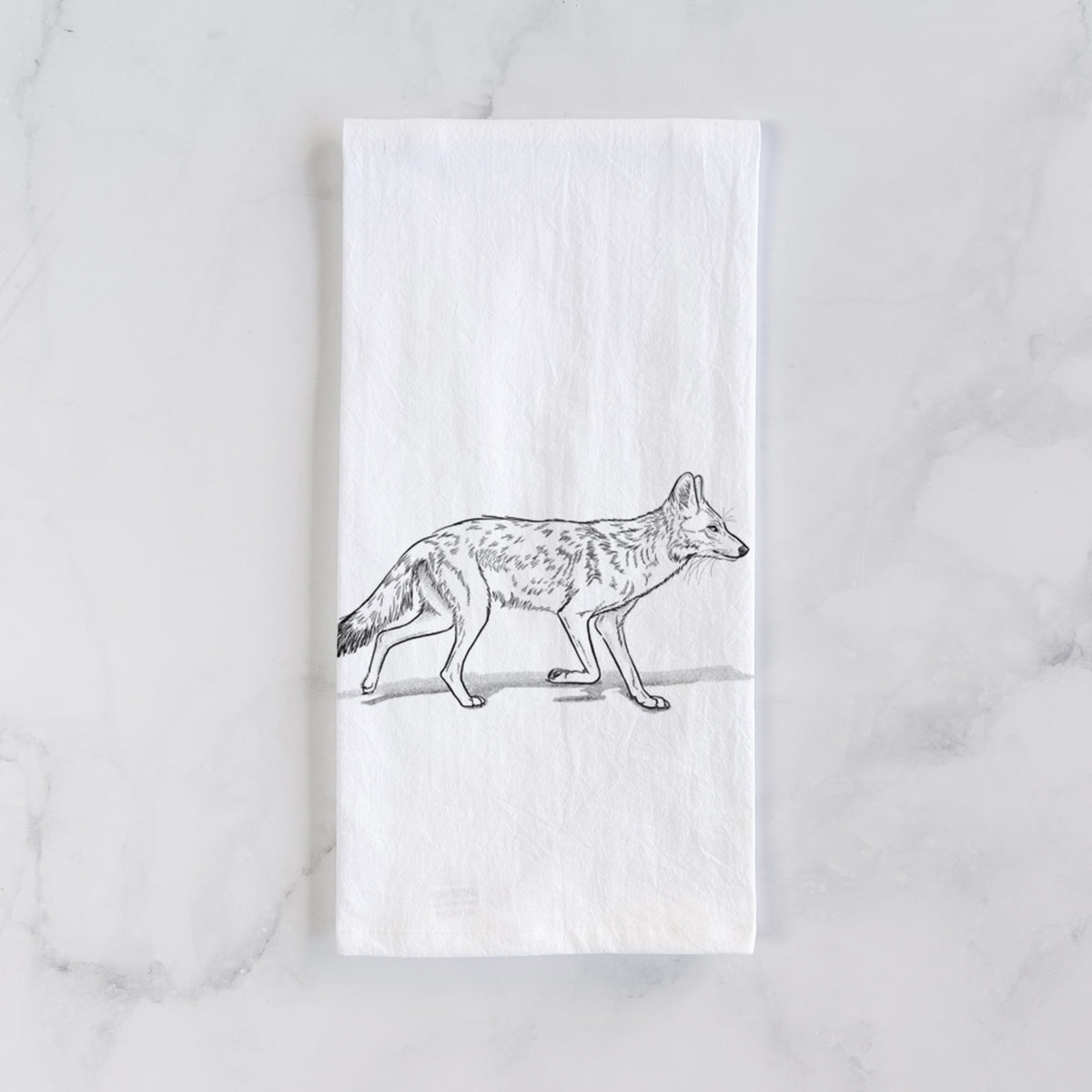 White cotton tea towel laid flat on marble, printed with a black ink illustration of a coyote trotting.