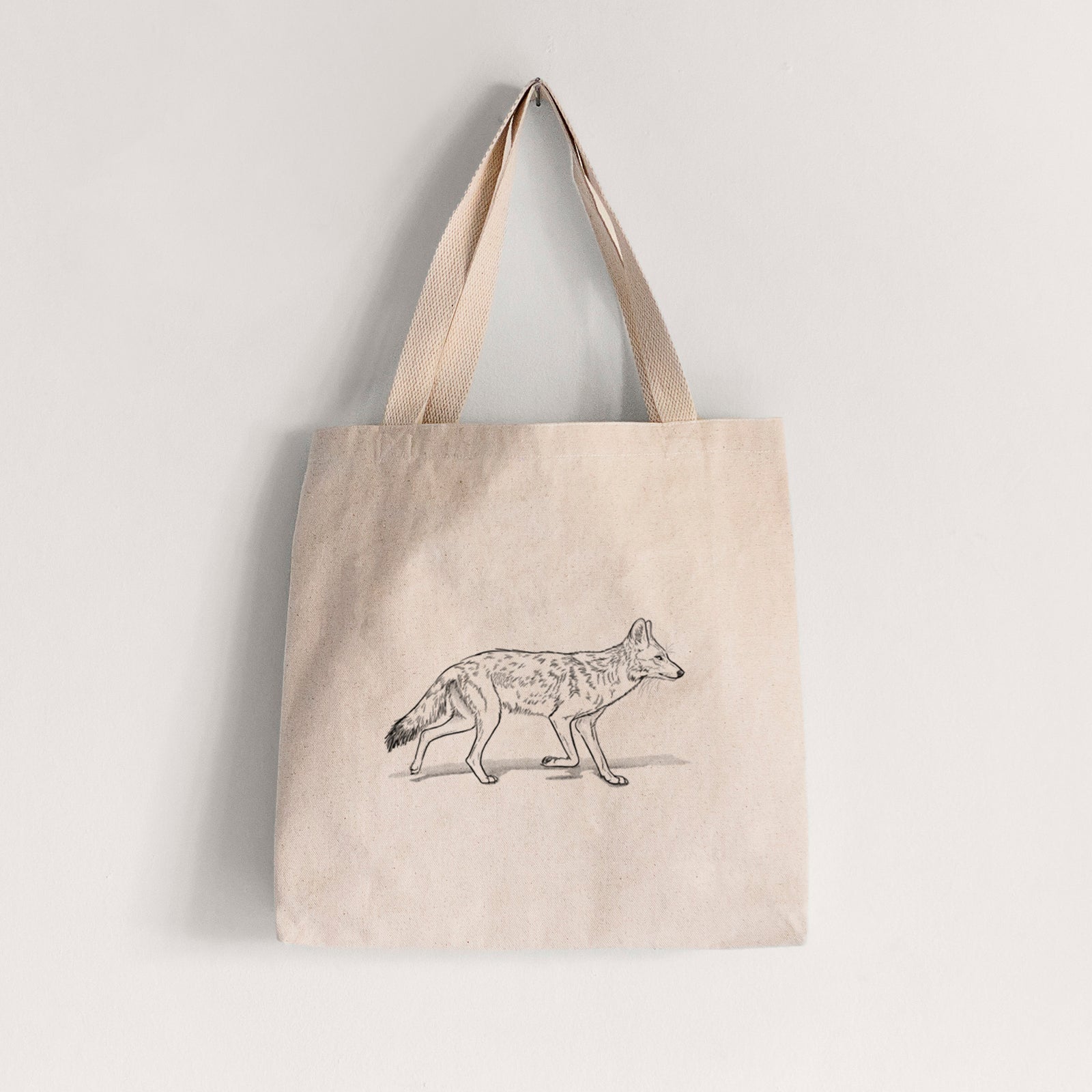 Natural canvas tote bag printed with a black ink illustration of a coyote trotting.
