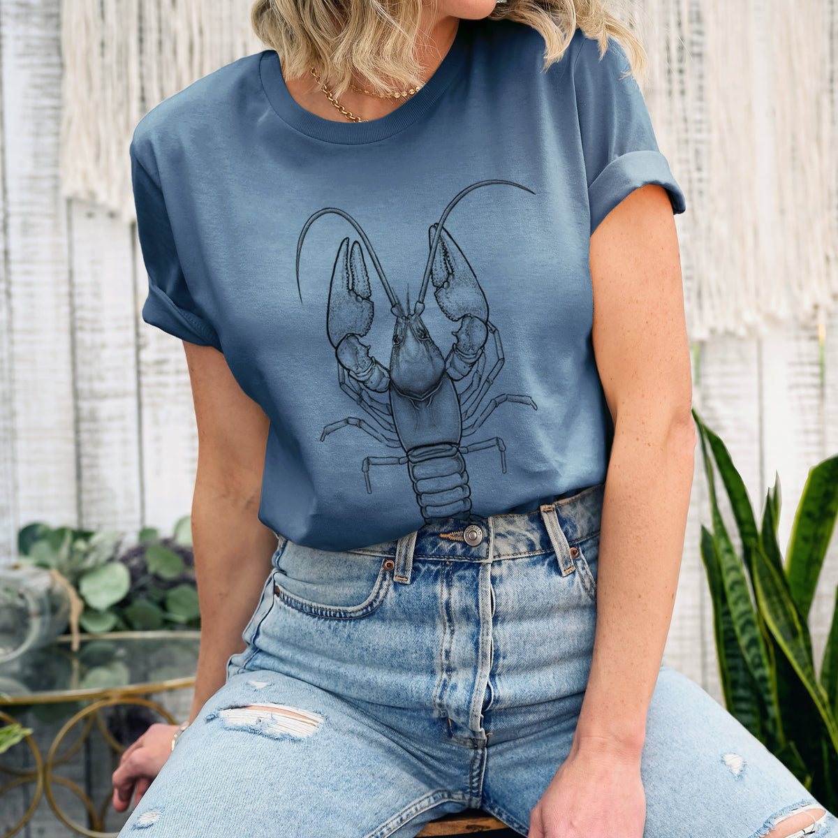 Woman wearing a steel blue lightweight cotton t-shirt printed with a detailed black ink illustration of a crayfish with its claws raised, seen from above.