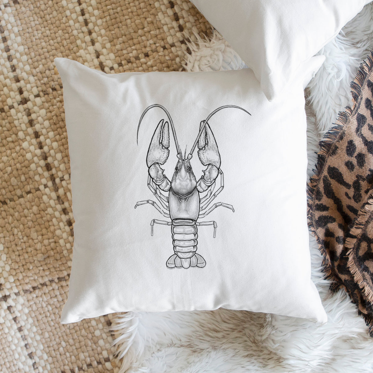 White pillow cover printed with a detailed black ink illustration of a crayfish with its claws raised, seen from above, on a woven chair.