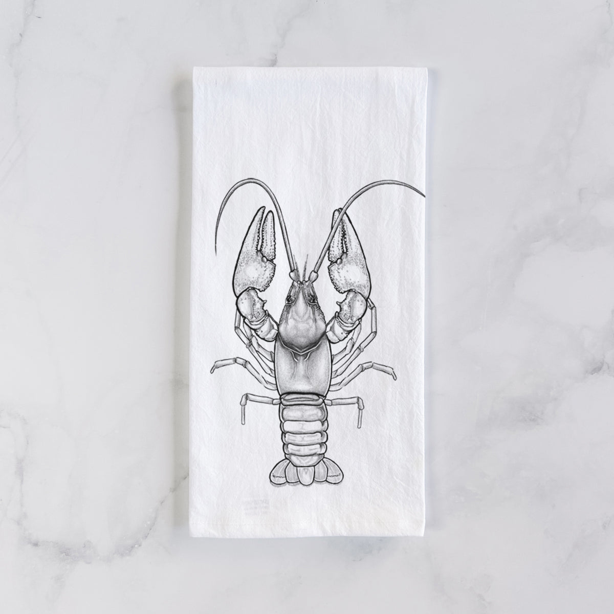 White cotton tea towel laid flat on marble, printed with a detailed black ink illustration of a crayfish with its claws raised, seen from above.