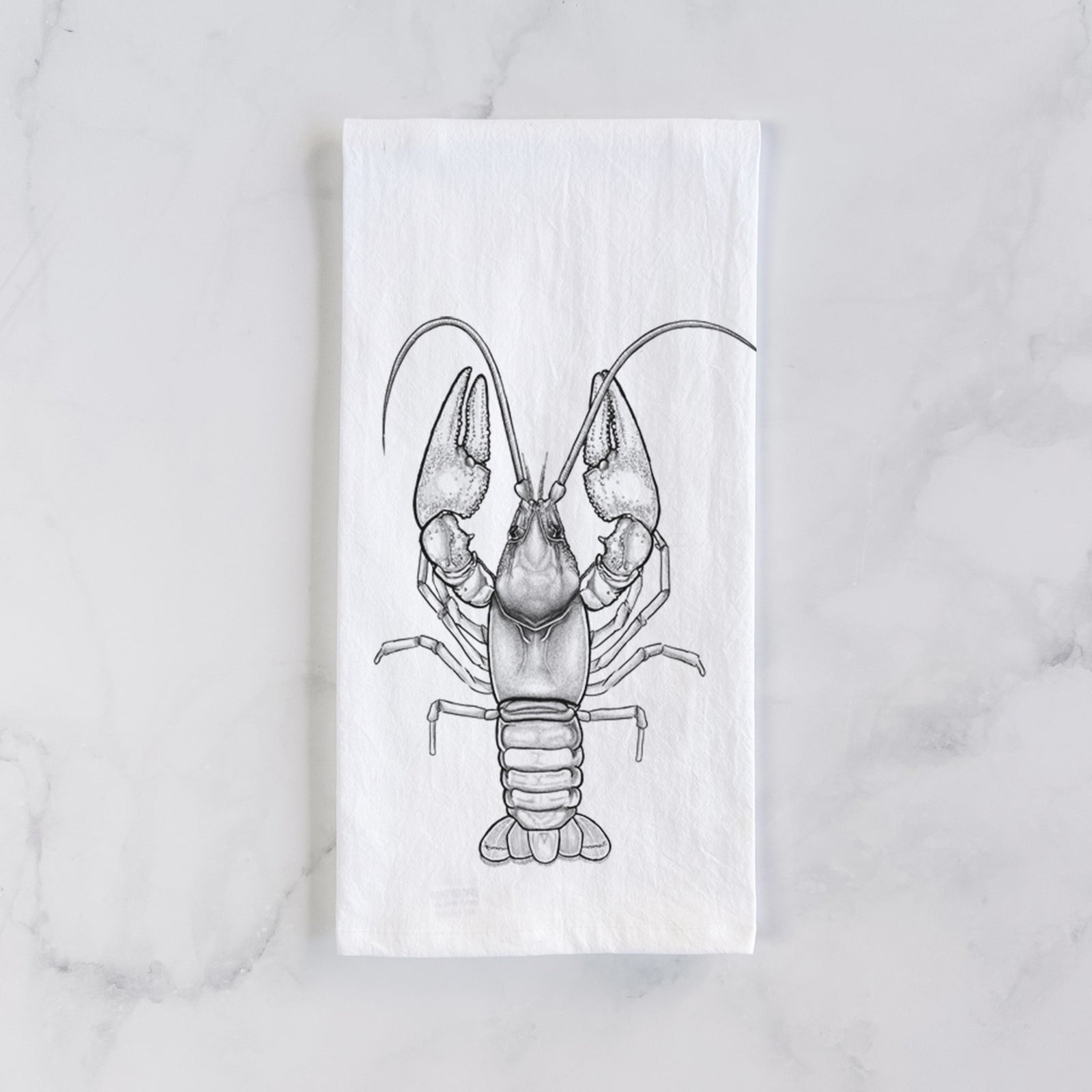 White cotton tea towel printed with a detailed black ink illustration of a crayfish with its claws raised, seen from above, on a marble counter beside a round wooden cutting board and greenery.