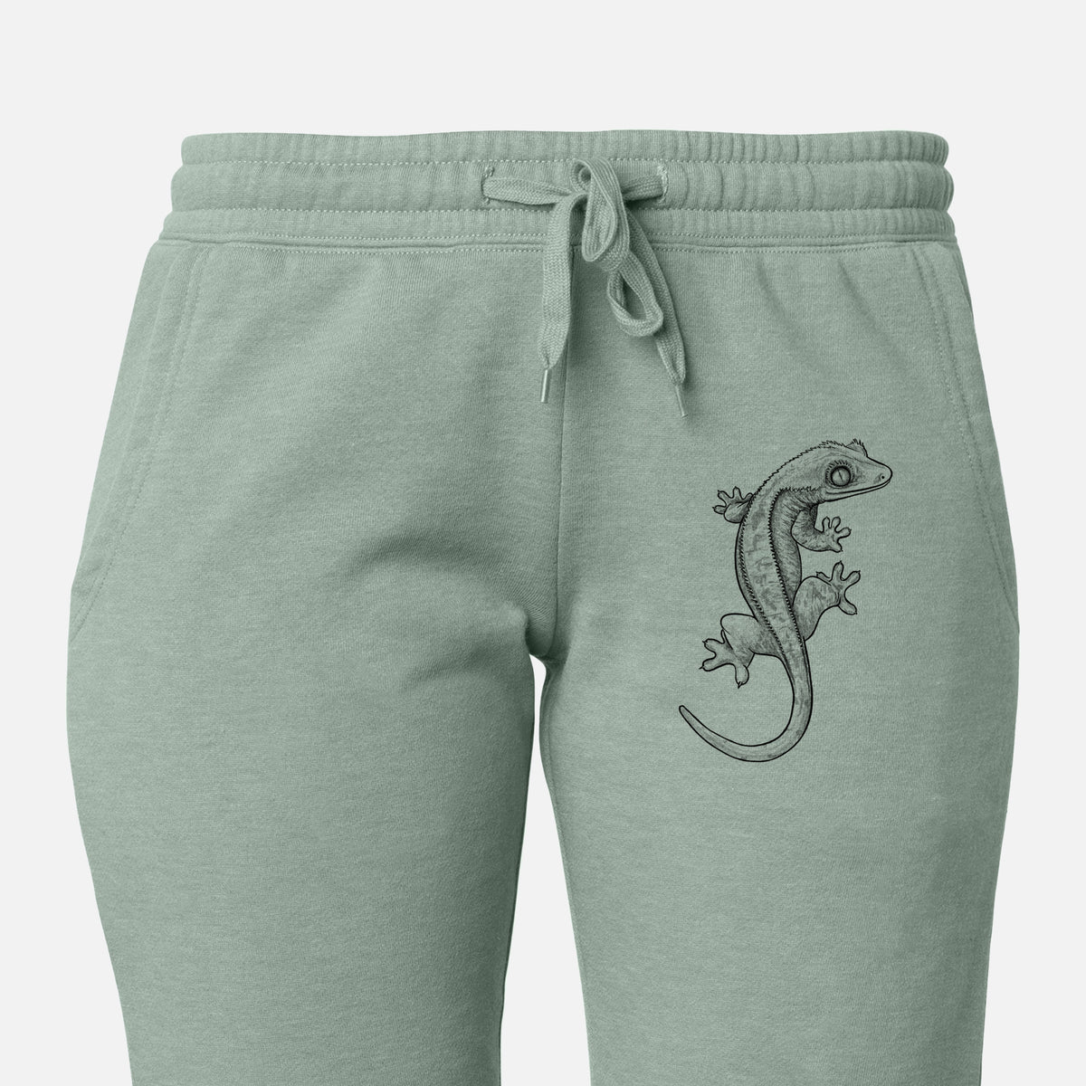 Front of sage green Cali Wave sweatpants, printed with a detailed black ink illustration of a crested gecko climbing on the leg.
