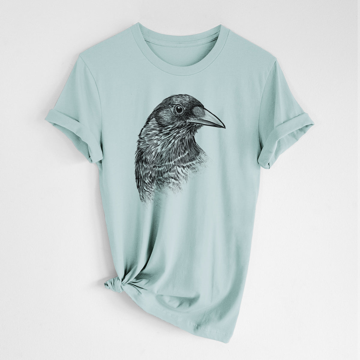 Dusty blue lightweight cotton t-shirt laid flat with the sleeves rolled, printed with a detailed black ink portrait of a crow's head in profile.