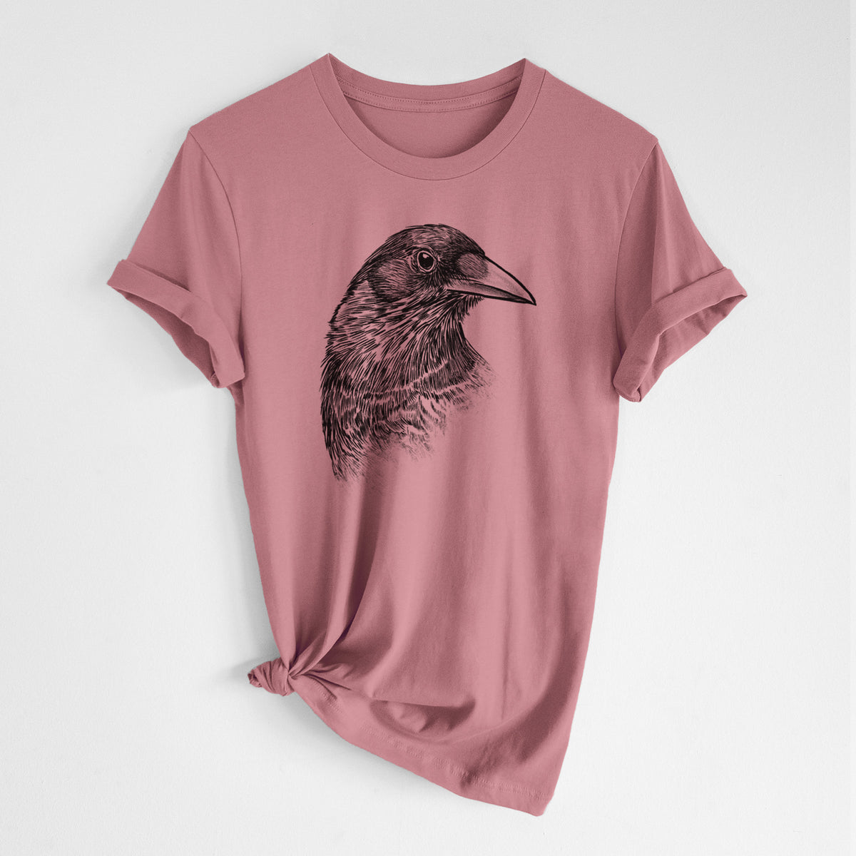 Mauve pink lightweight cotton t-shirt laid flat with the sleeves rolled, printed with a detailed black ink portrait of a crow's head in profile.