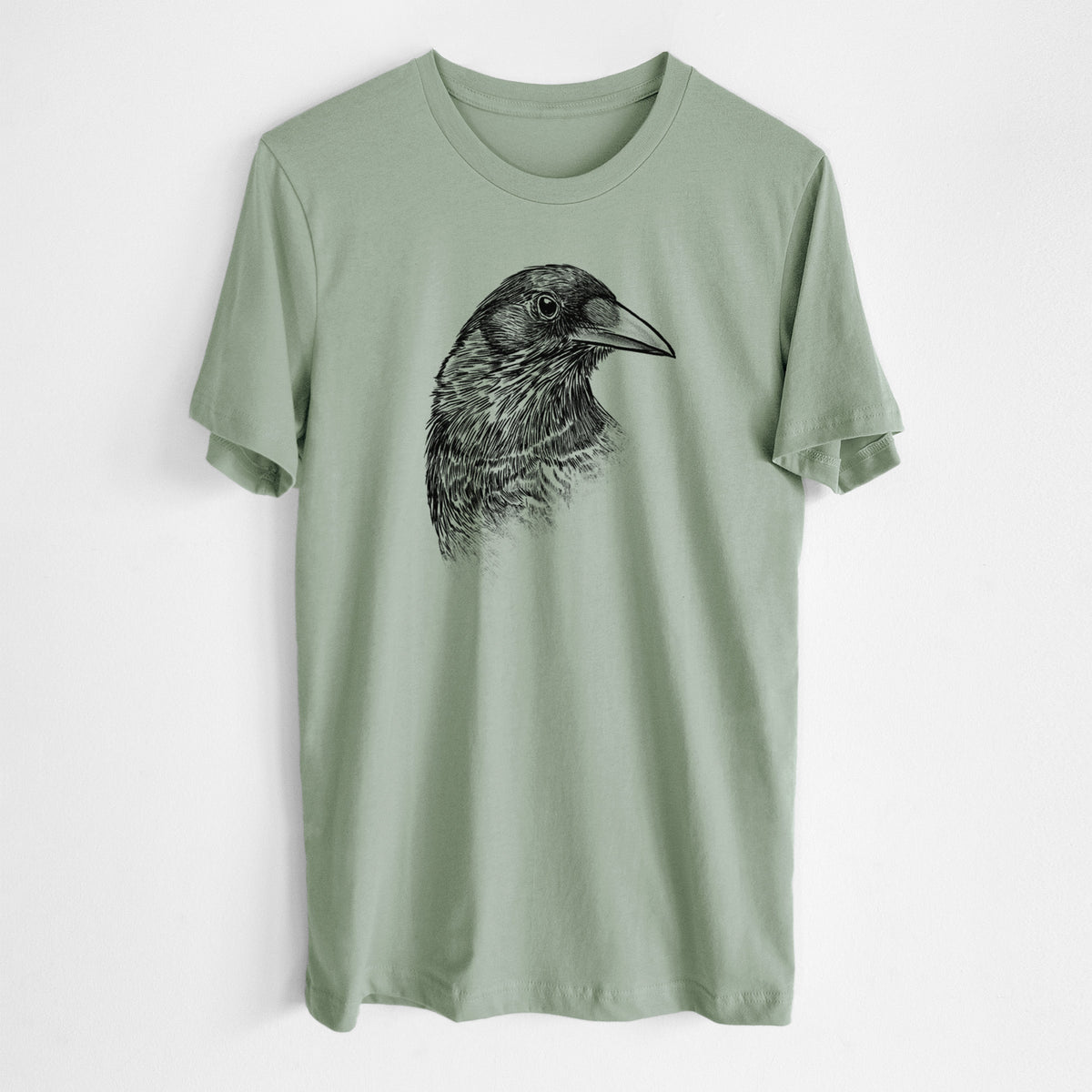 Sage green lightweight cotton t-shirt laid flat, printed with a detailed black ink portrait of a crow's head in profile.