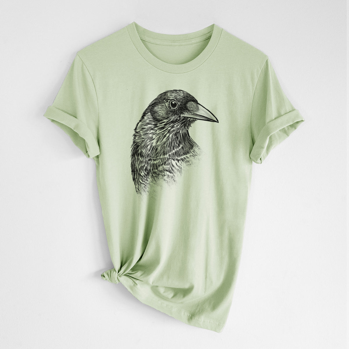 Spring green lightweight cotton t-shirt laid flat with the sleeves rolled, printed with a detailed black ink portrait of a crow's head in profile.