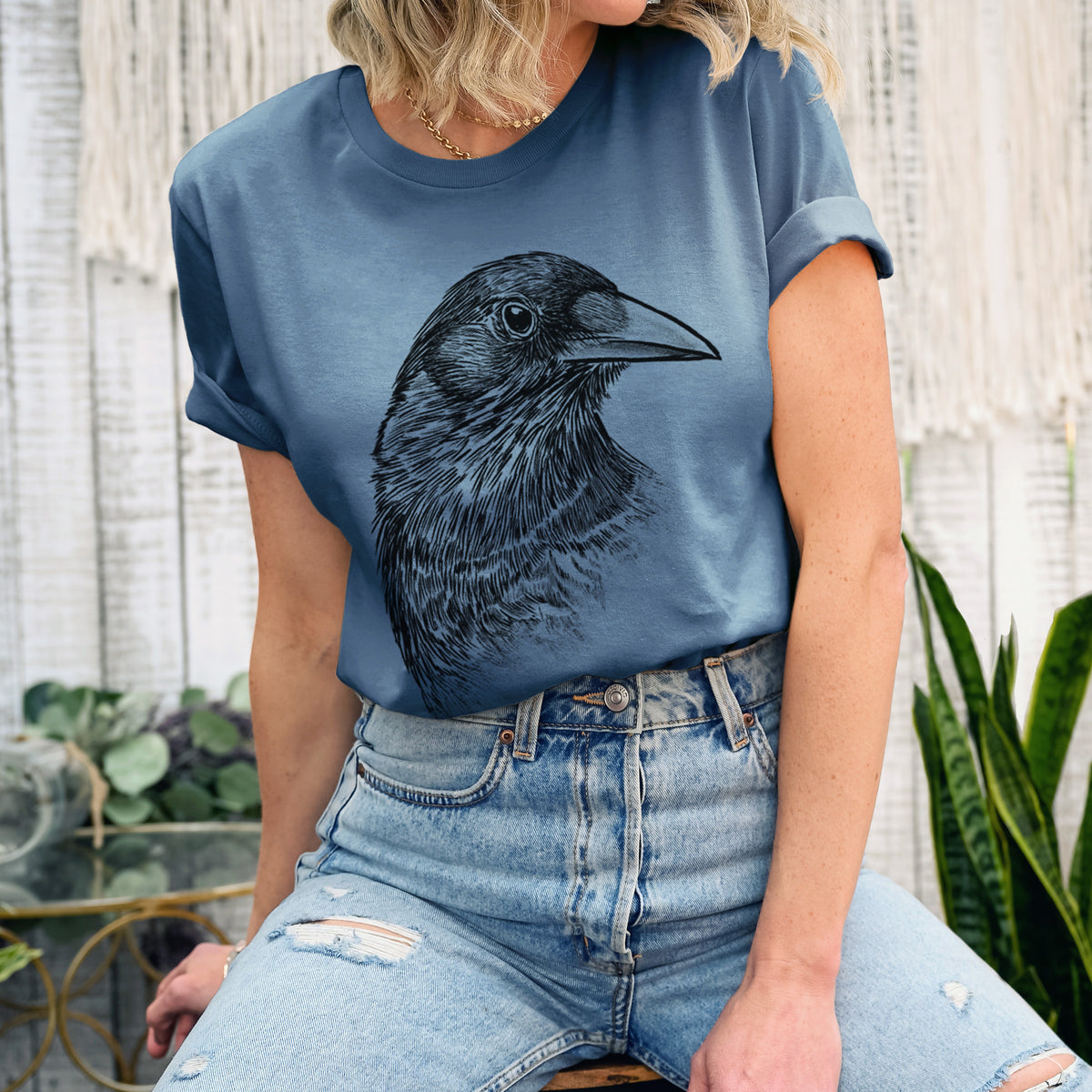 Woman wearing a steel blue lightweight cotton t-shirt printed with a detailed black ink portrait of a crow's head in profile.
