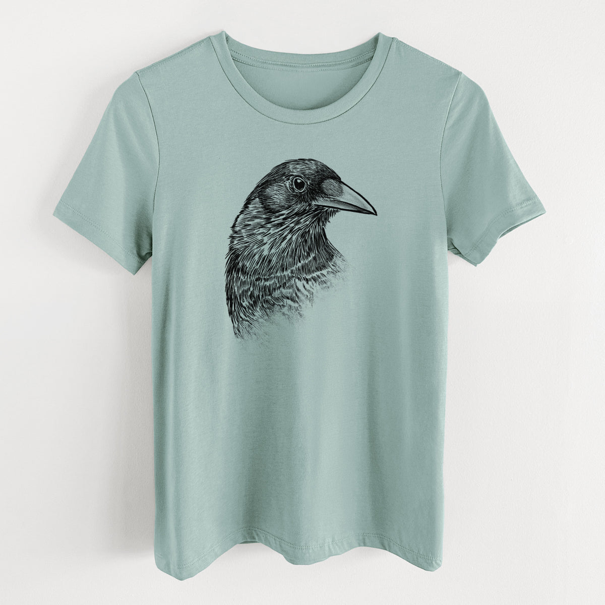 Dusty blue women's relaxed fit cotton t-shirt laid flat, printed with a detailed black ink portrait of a crow's head in profile.