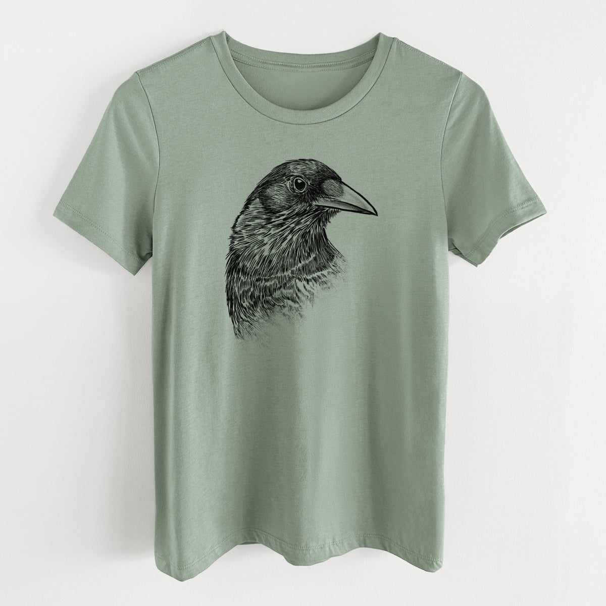 Sage green women's relaxed fit cotton t-shirt laid flat, printed with a detailed black ink portrait of a crow's head in profile.