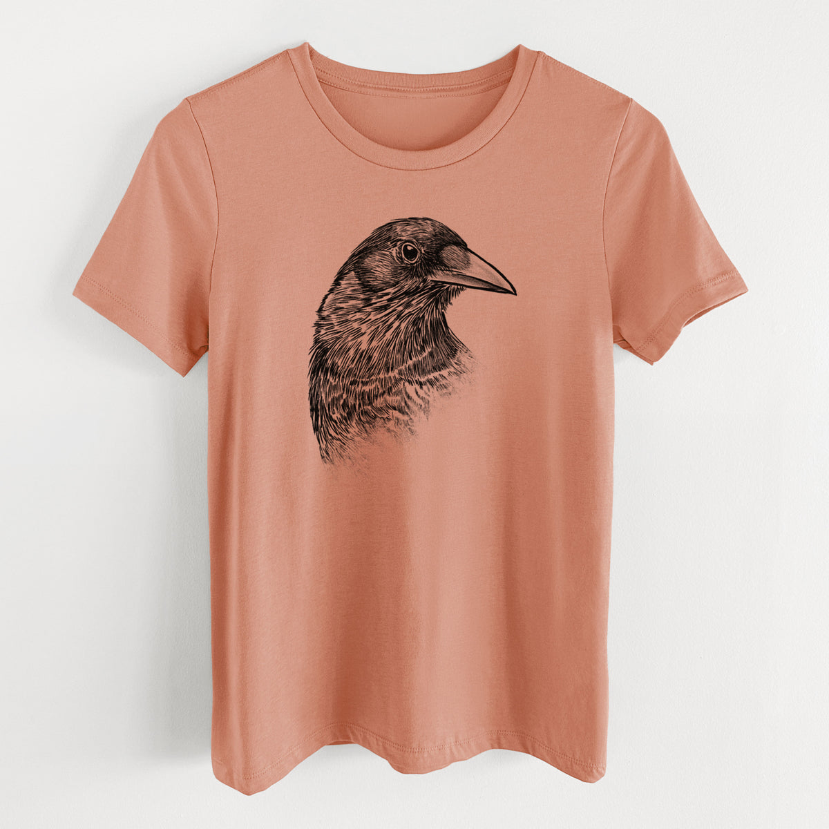 Terracotta orange women's relaxed fit cotton t-shirt laid flat, printed with a detailed black ink portrait of a crow's head in profile.