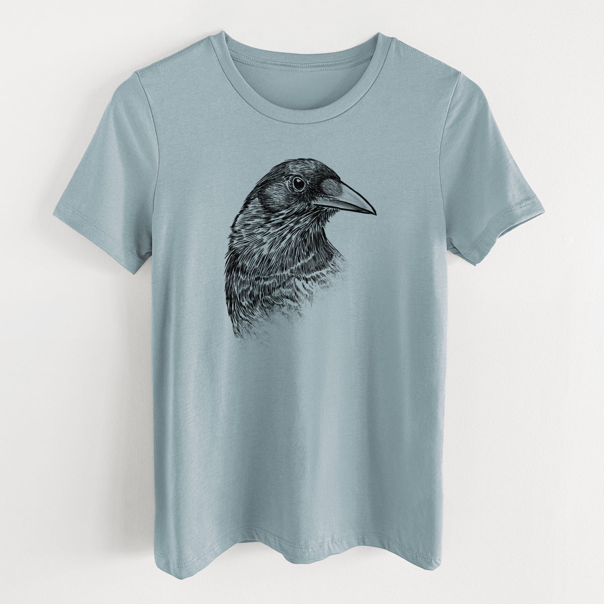 Vintage denim women's relaxed fit cotton t-shirt laid flat, printed with a detailed black ink portrait of a crow's head in profile.