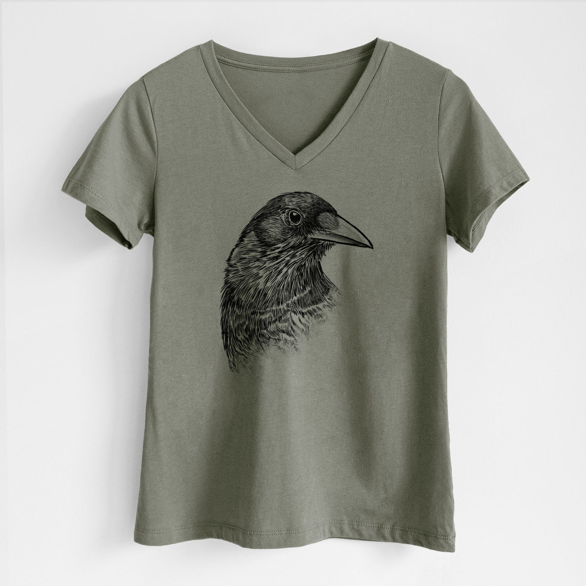 Military green women's relaxed fit cotton V-neck t-shirt laid flat, printed with a detailed black ink portrait of a crow's head in profile.