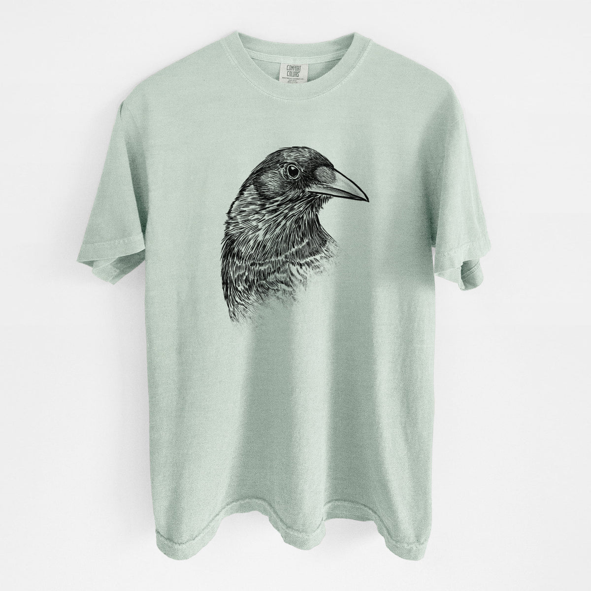 Bay green Comfort Colors t-shirt laid flat, printed with a detailed black ink portrait of a crow's head in profile.