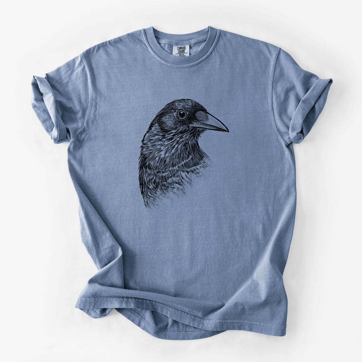 Blue jean Comfort Colors t-shirt laid flat, printed with a detailed black ink portrait of a crow's head in profile.