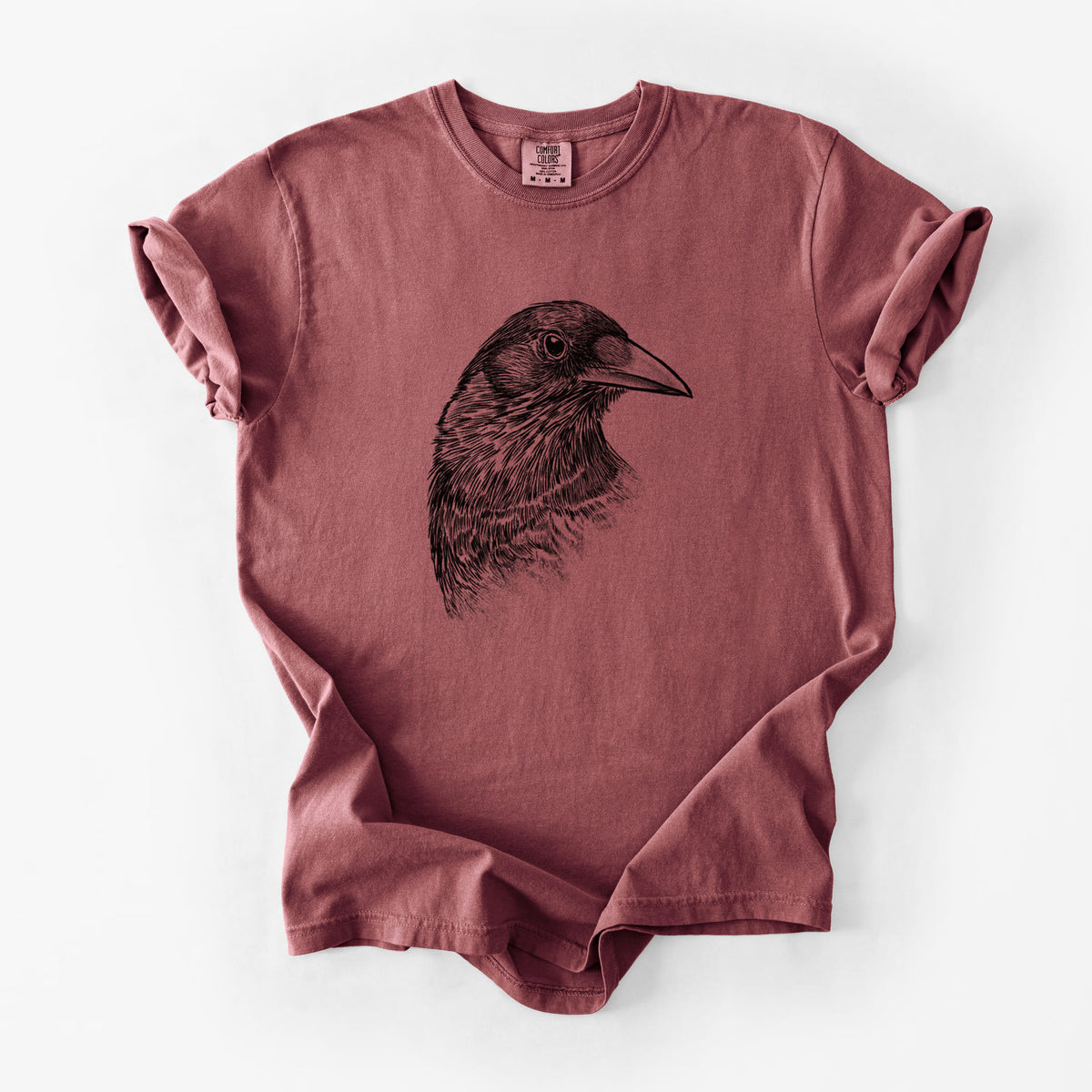 Brick red Comfort Colors t-shirt laid flat, printed with a detailed black ink portrait of a crow's head in profile.