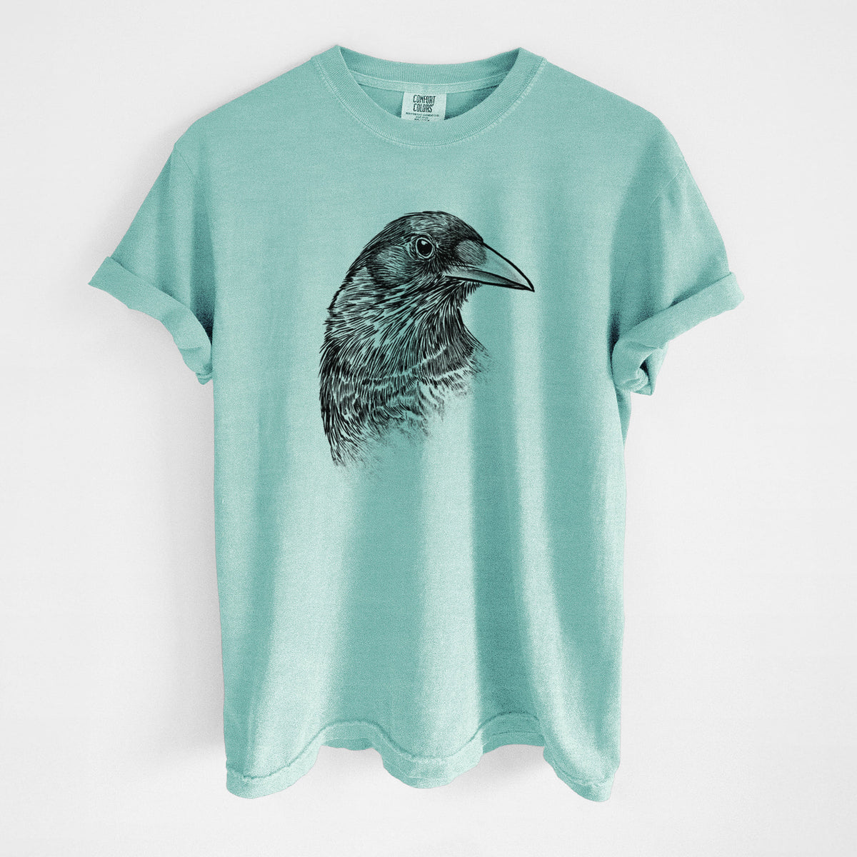 Chalky mint Comfort Colors t-shirt laid flat, printed with a detailed black ink portrait of a crow's head in profile.