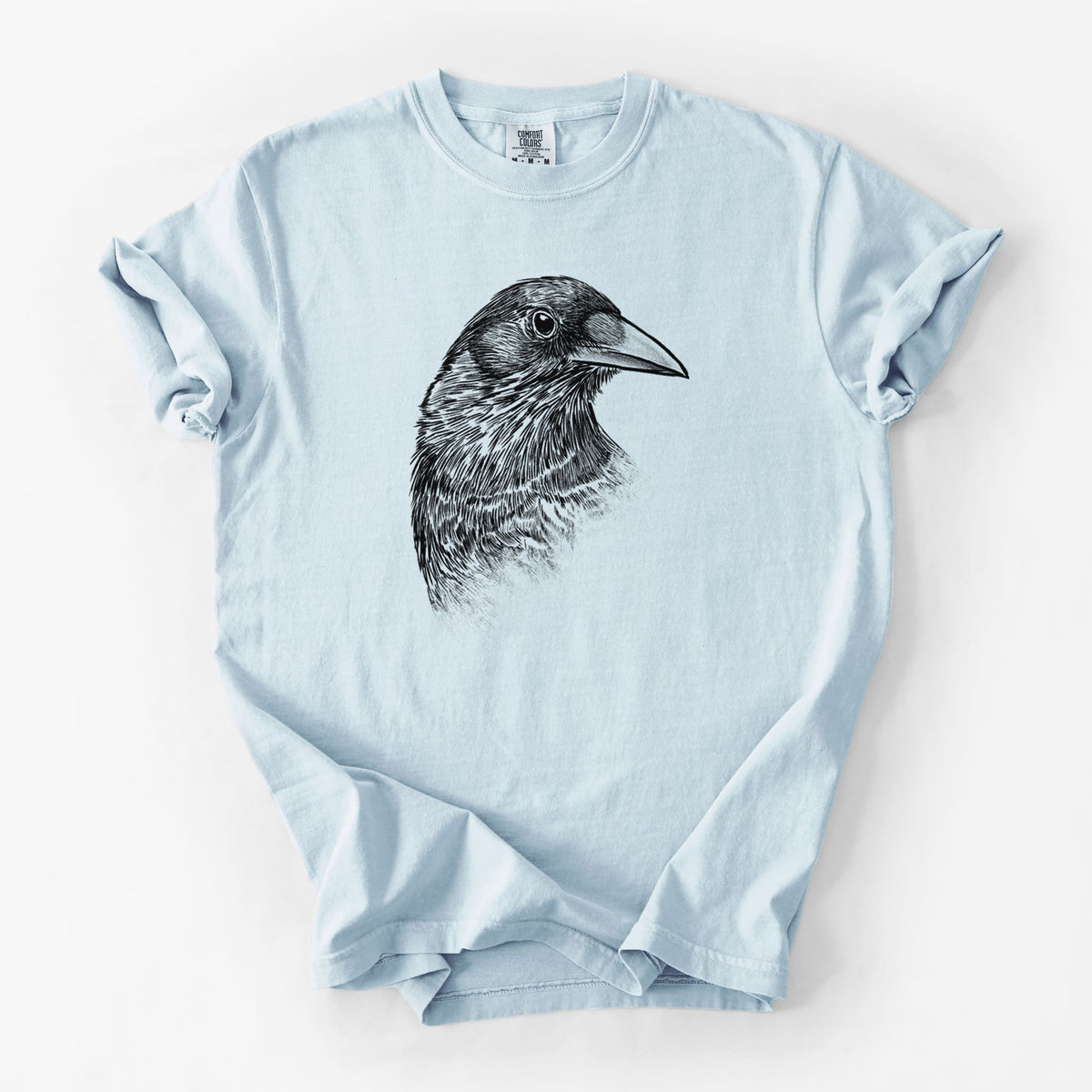 Chambray blue Comfort Colors t-shirt laid flat, printed with a detailed black ink portrait of a crow's head in profile.