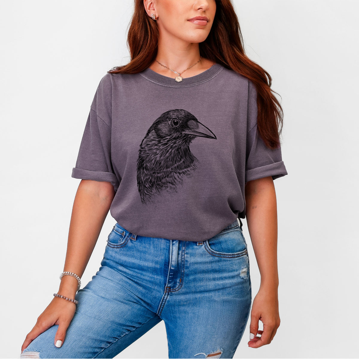 Woman wearing a Comfort Colors t-shirt printed with a detailed black ink portrait of a crow's head in profile.