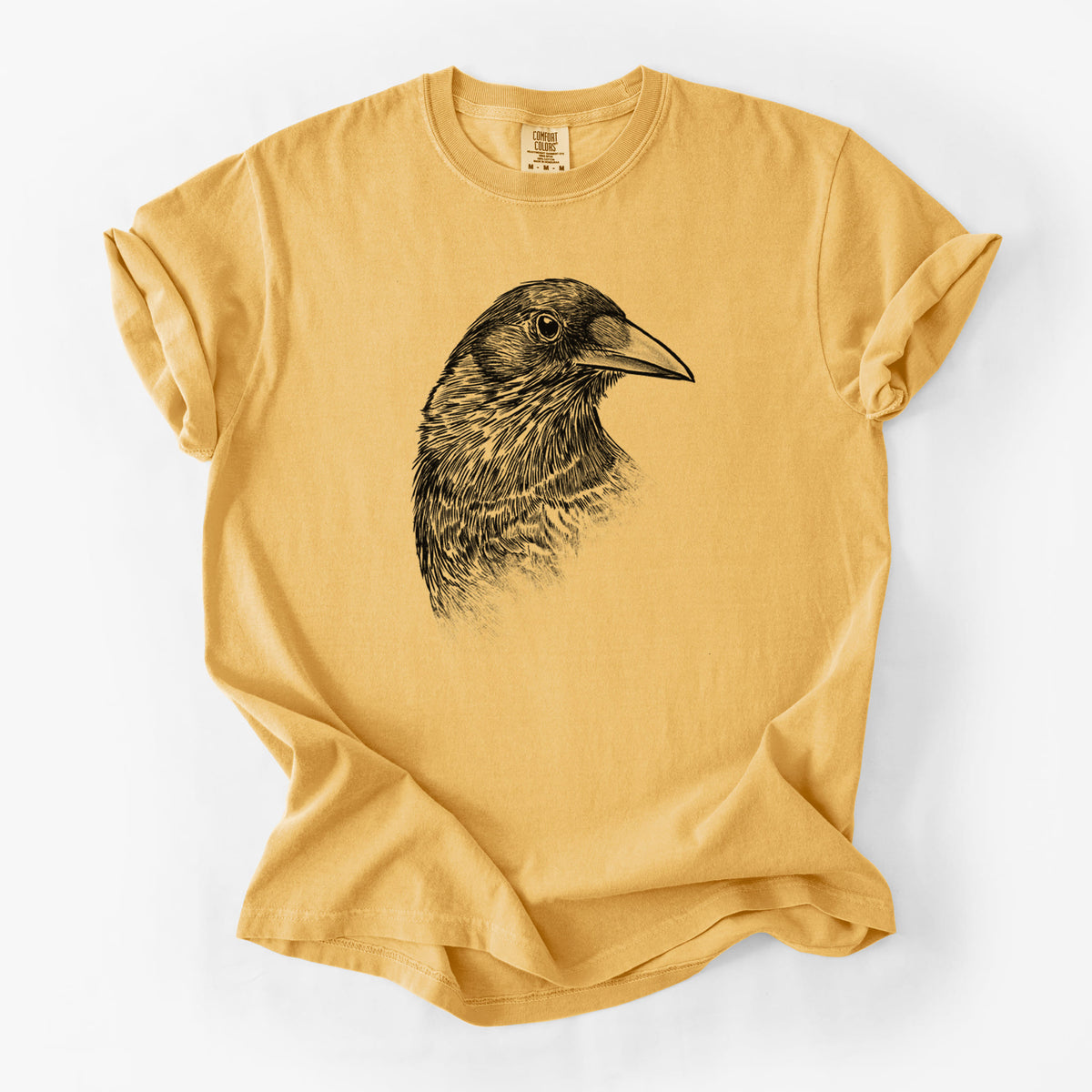 Golden wheat yellow Comfort Colors t-shirt laid flat, printed with a detailed black ink portrait of a crow's head in profile.