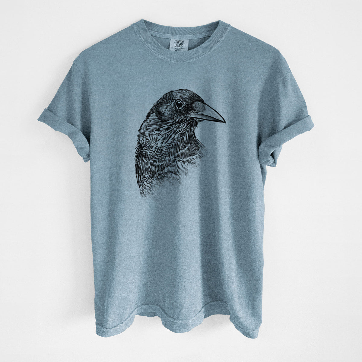 Steel blue Comfort Colors t-shirt laid flat, printed with a detailed black ink portrait of a crow's head in profile.