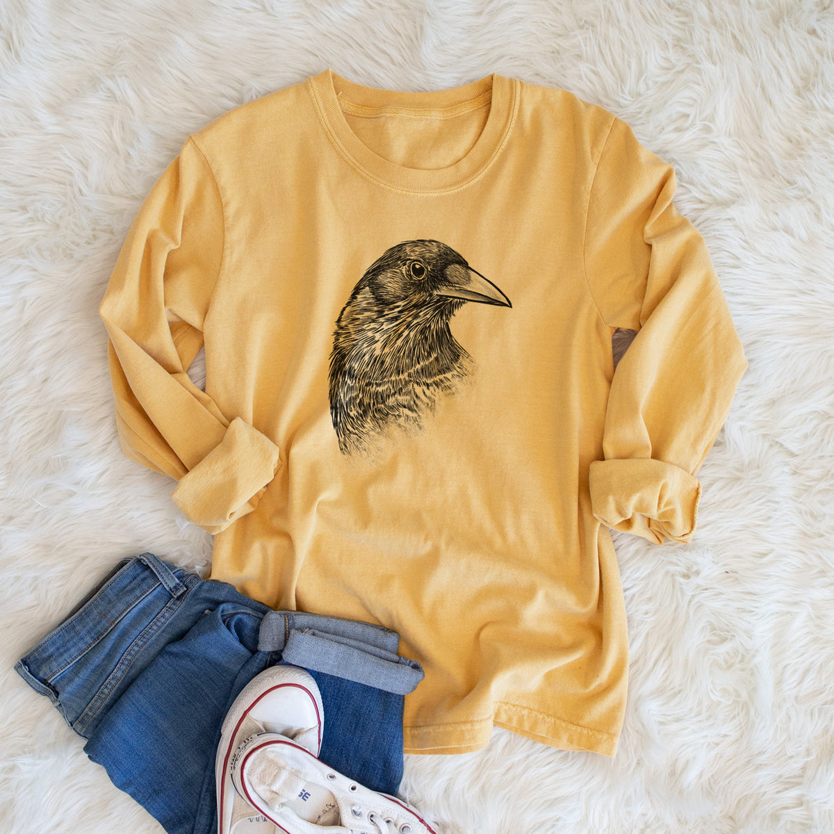 Golden wheat yellow Comfort Colors long sleeve shirt printed with a detailed black ink portrait of a crow's head in profile, shown in a lifestyle photo.