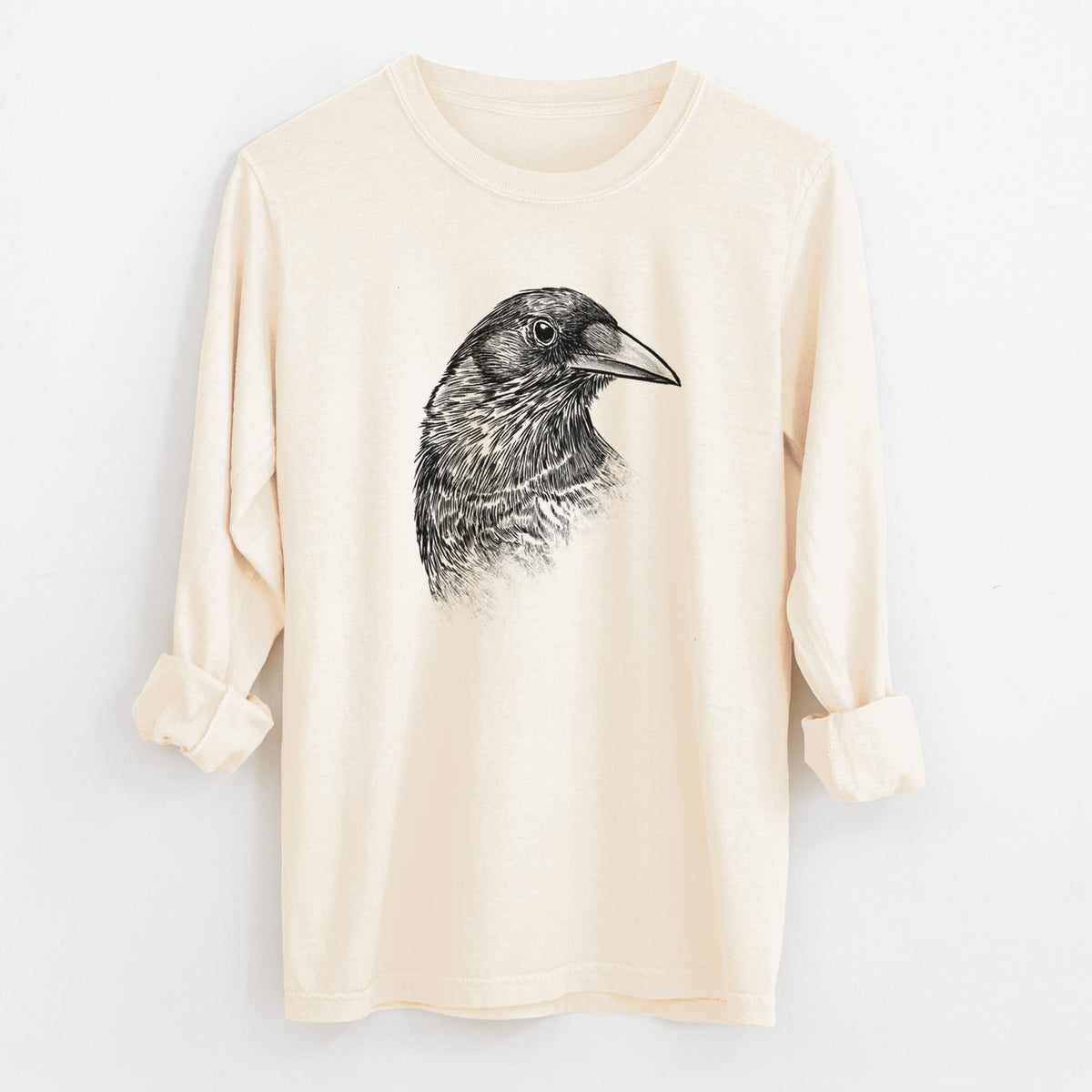 Ivory Comfort Colors long sleeve shirt laid flat with the cuffs rolled, printed with a detailed black ink portrait of a crow's head in profile.