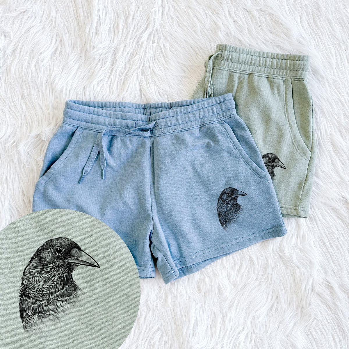 Two pairs of Cali Wave shorts in different colors printed with a detailed black ink portrait of a crow's head in profile, with a close-up of the print.
