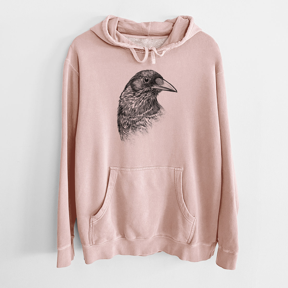 Dusty pink pigment dyed hoodie laid flat, printed with a detailed black ink portrait of a crow's head in profile.