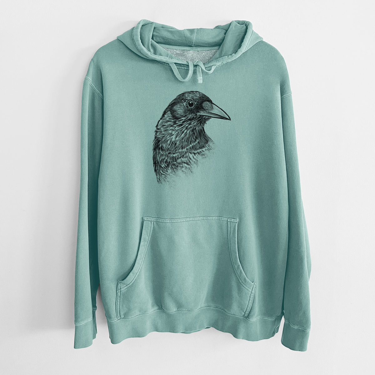 Mint green pigment dyed hoodie laid flat, printed with a detailed black ink portrait of a crow's head in profile.