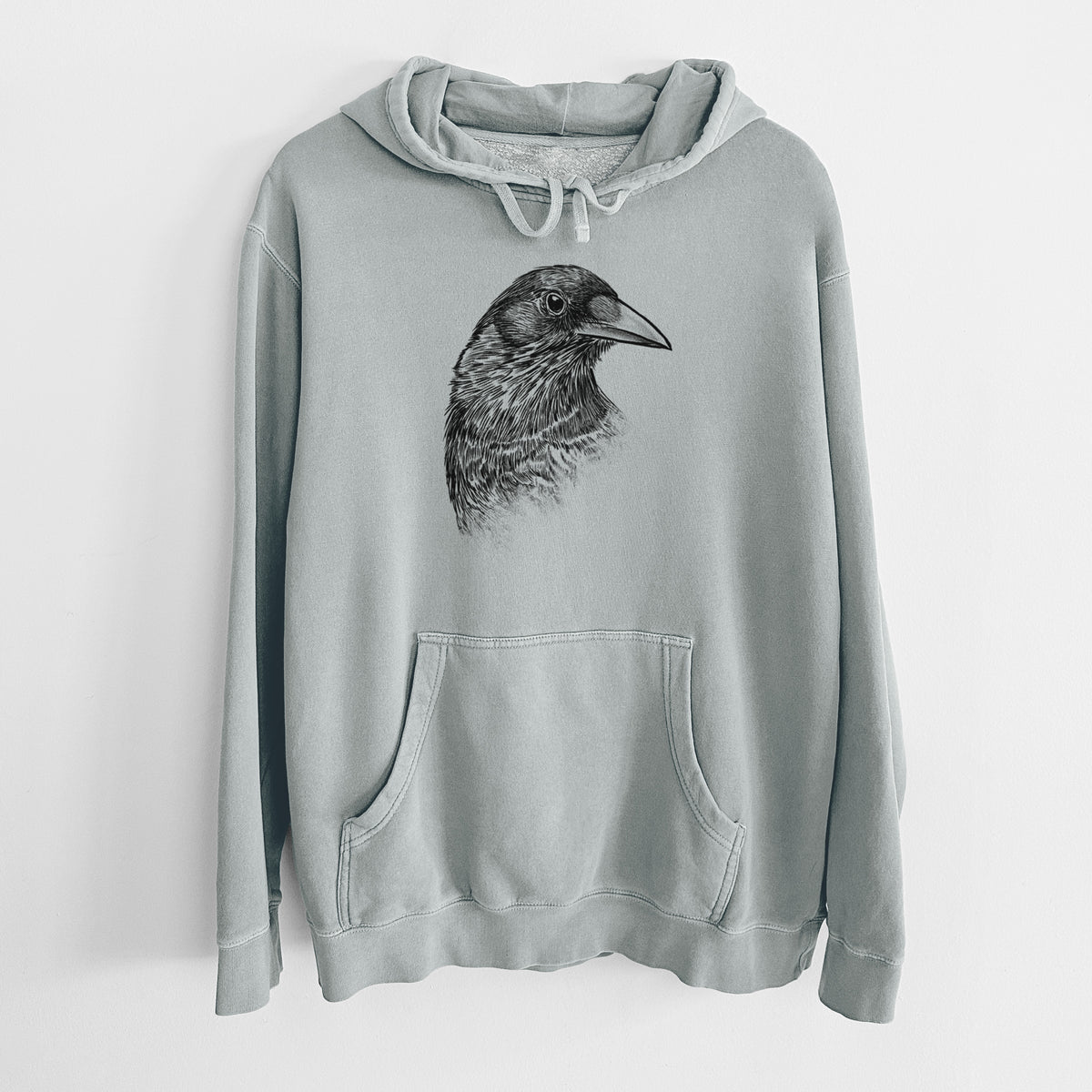 Sage green pigment dyed hoodie laid flat, printed with a detailed black ink portrait of a crow's head in profile.