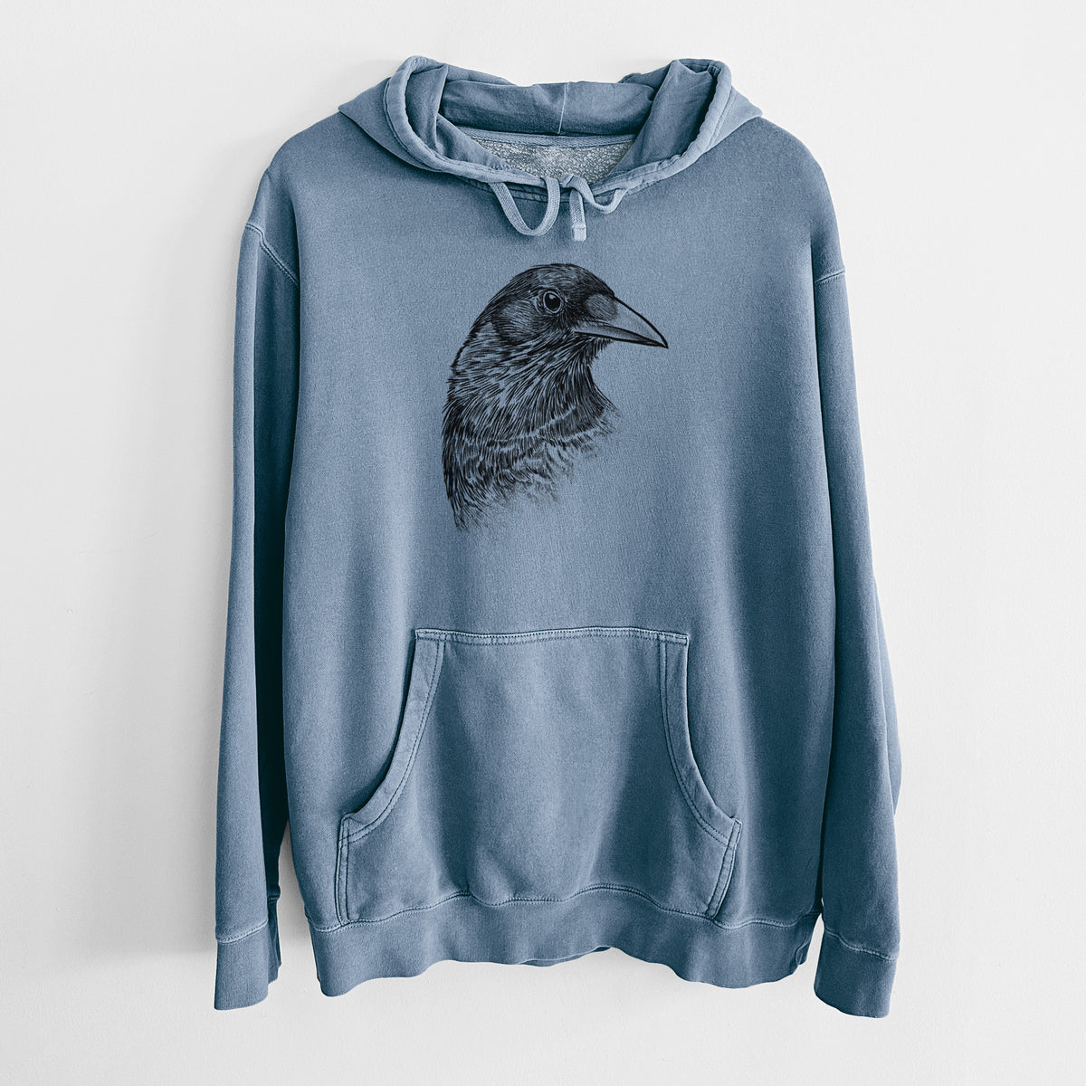 Slate blue pigment dyed hoodie laid flat, printed with a detailed black ink portrait of a crow's head in profile.