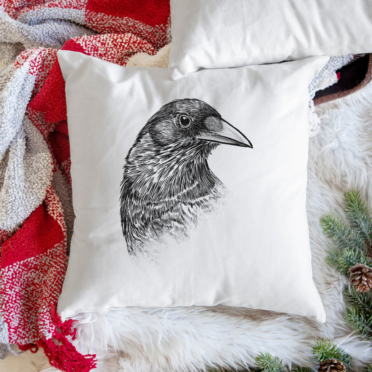 White pillow cover printed with a detailed black ink portrait of a crow's head in profile, on a woven chair.