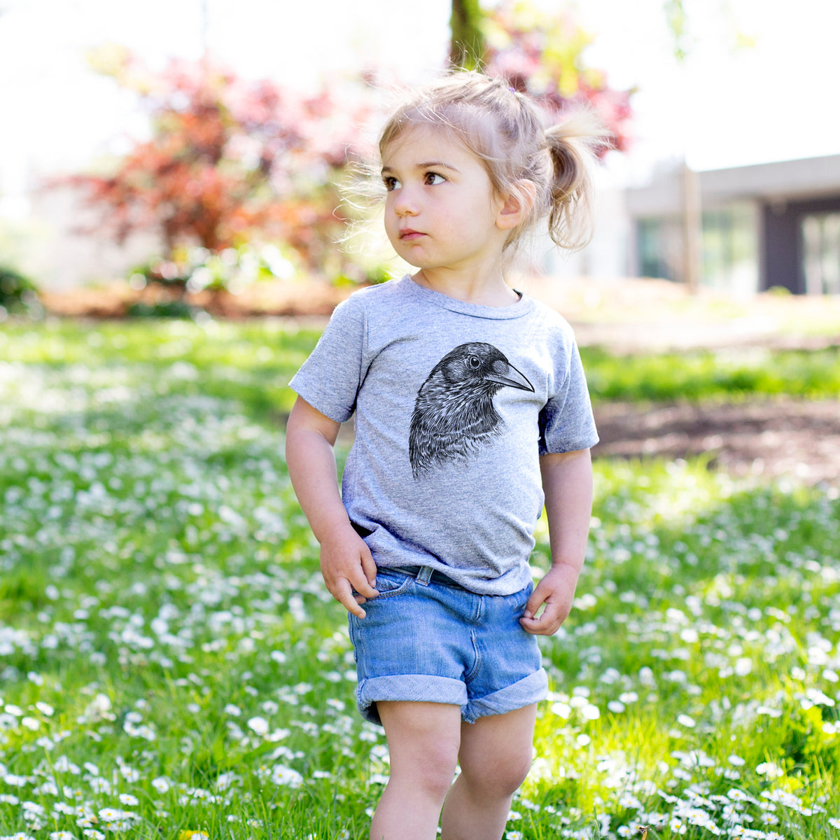 Toddler girl walking outdoors wearing a t-shirt printed with a detailed black ink portrait of a crow's head in profile.