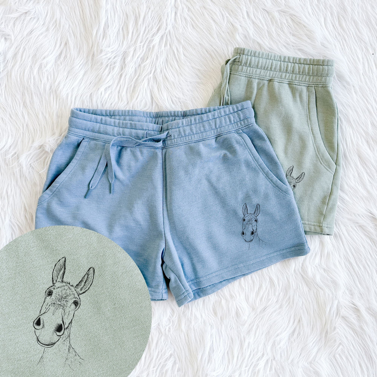 Two pairs of Cali Wave shorts in different colors printed with a black ink illustration of a curious donkey's head with tall ears, with a close-up of the print.