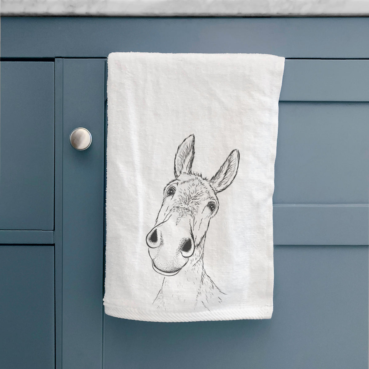 White hand towel printed with a black ink illustration of a curious donkey's head with tall ears, hanging on a cabinet door.