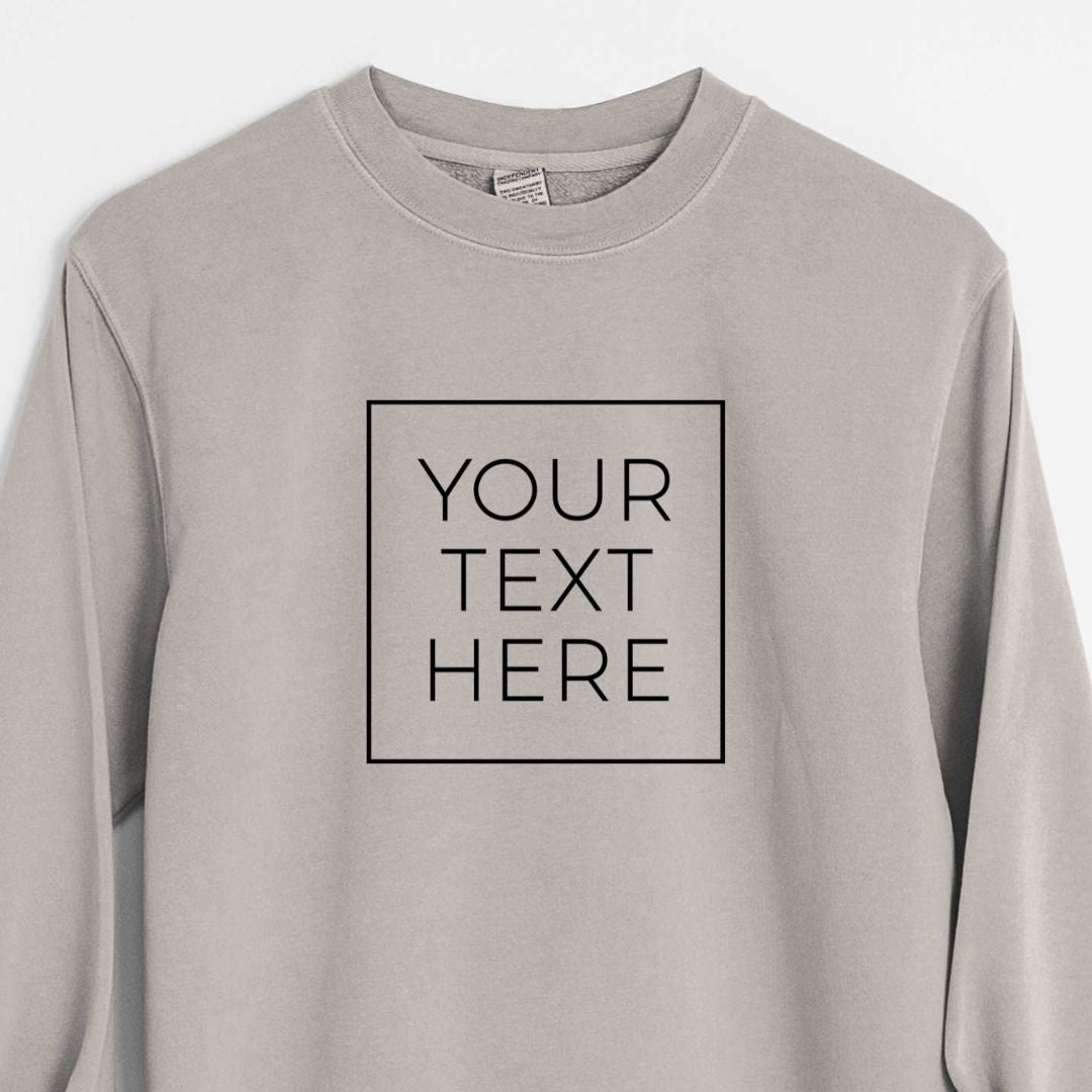 Cement grey pigment dyed crewneck sweatshirt laid flat with the sleeves rolled, printed with your own custom text in black letters inside a square outline.