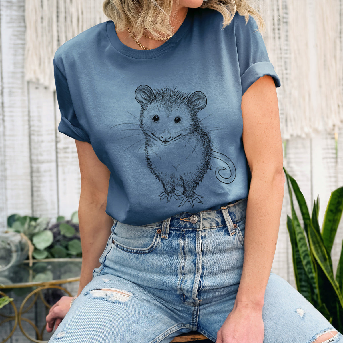 Woman wearing a steel blue lightweight cotton t-shirt printed with a black ink illustration of a wide-eyed baby opossum sitting.